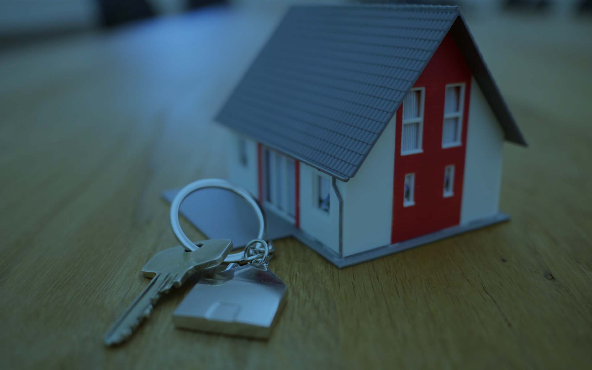 A small model house with a red door and a set of keys on a wooden surface.